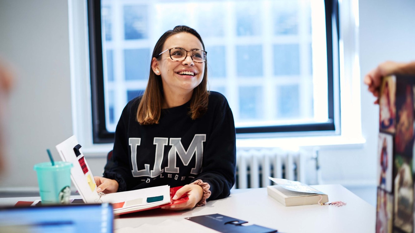 female student in LIM sweathshirt sitting in a classroom with a swatch book opened