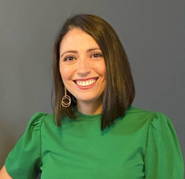 LIM alum Anna Bennudriti wears a green shirt against and smiles.