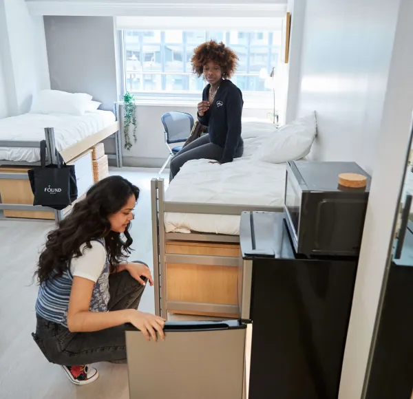 students sitting on bed and opening fridge