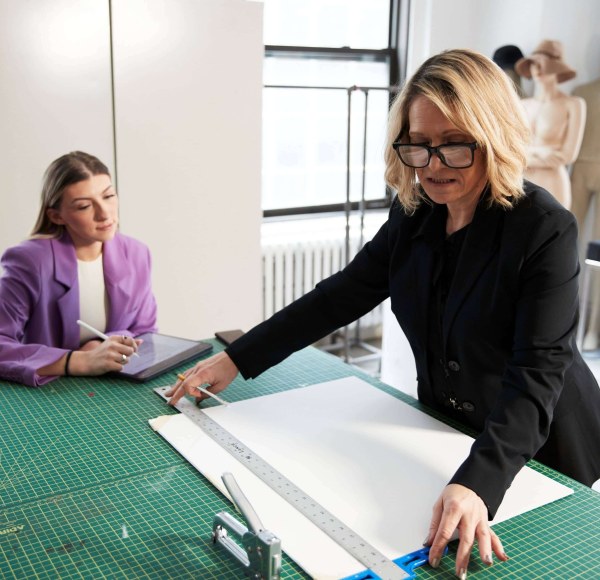 LIM professor Monica Rakocy measures a length of a poster board while a student takes notes