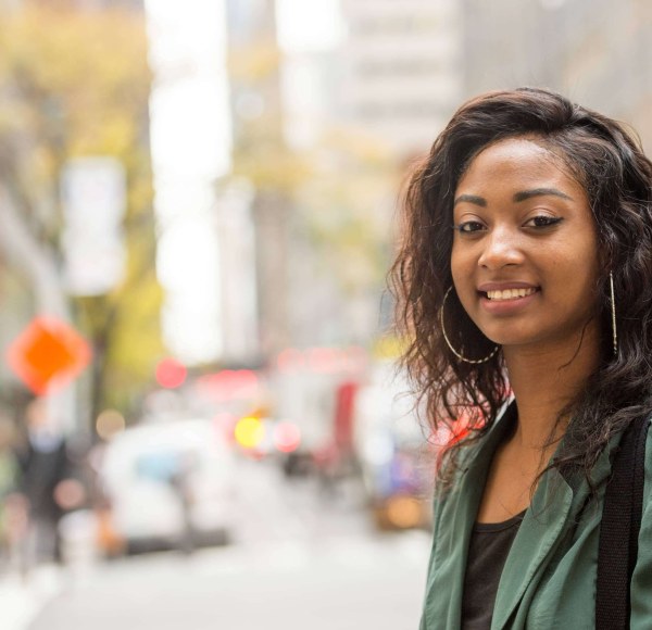 An LIM student with a green shirt and large hoop earrings poses in the streets of New York City