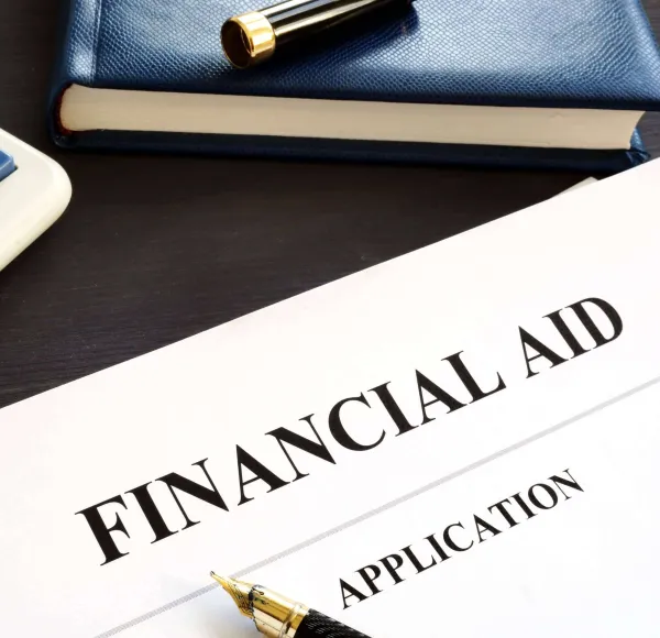 A financial aid application sits on a desk with a pen, calculator, and notebook nearby