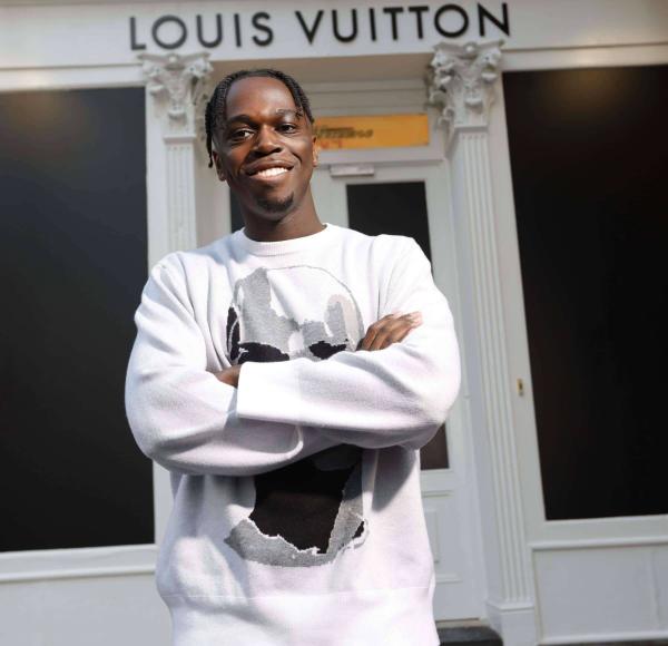A Male student crosses his arm and smiles while standing in front of Louis Vuitton in SoHo.