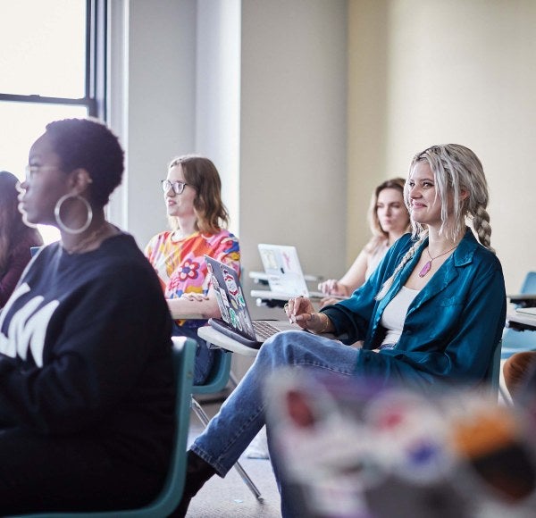 Students sit in classroom with laptops on their desktops