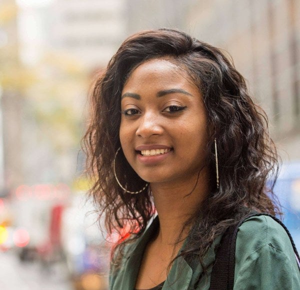 An LIM student with a green shirt and large hoop earrings poses in the streets of New York City