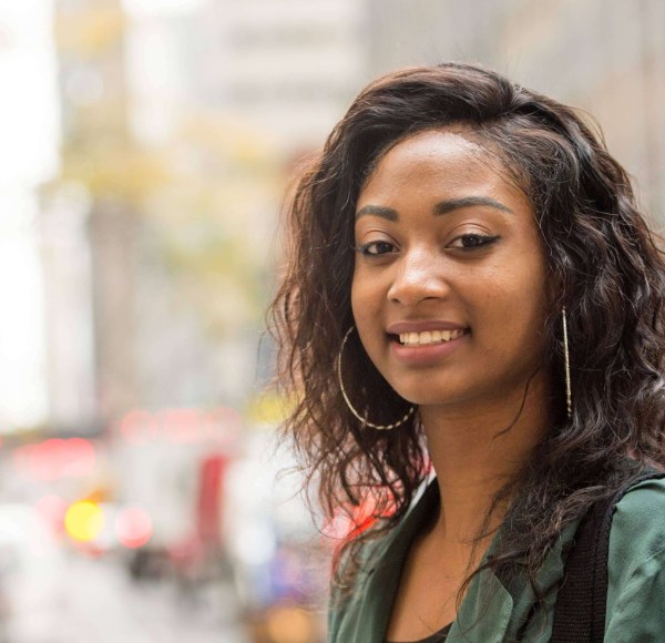 An LIM student with a green shirt and large hoop earrings poses in the streets of New York City