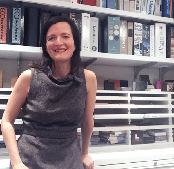 LIM professor Leonora Loeb wear a grey dress and stands in front of bookshelves