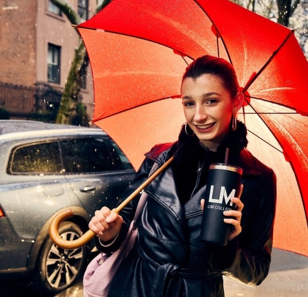 young woman, light-brown hair, leather coat, LIM beverage container, red umbrella, walks down the street in Brooklyn, New York.