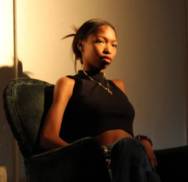 young women dressed in black since in padded easy chair against a light wall