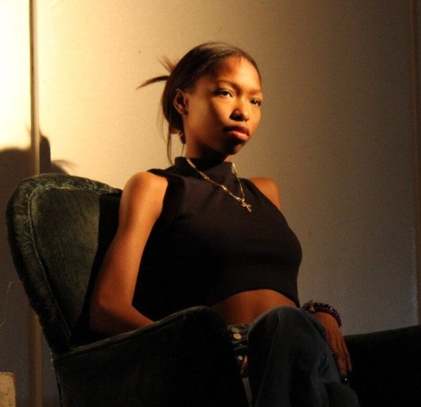 young women dressed in black since in padded easy chair against a light wall