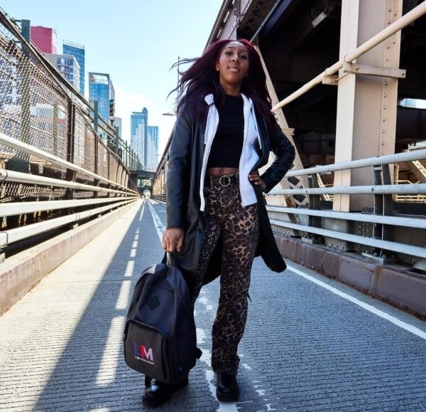 woman, long dark hair, leopard-print pants, LIM backpack, stands confidently on the 59th Street Bridge in New York