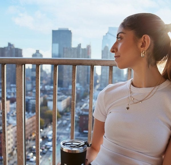 young woman, light-brown hair, beverage, balcony overlooking NYC