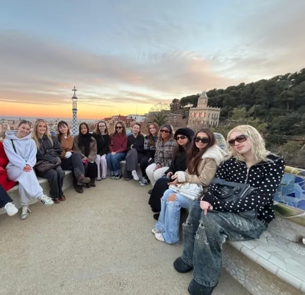 a group of students, dressed casually, sit on a rock bench in Park Guell in Barcelona, Spain