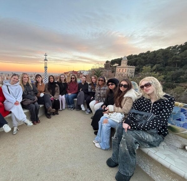 a group of students, dressed casually, sit on a rock bench in Park Guell in Barcelona, Spain