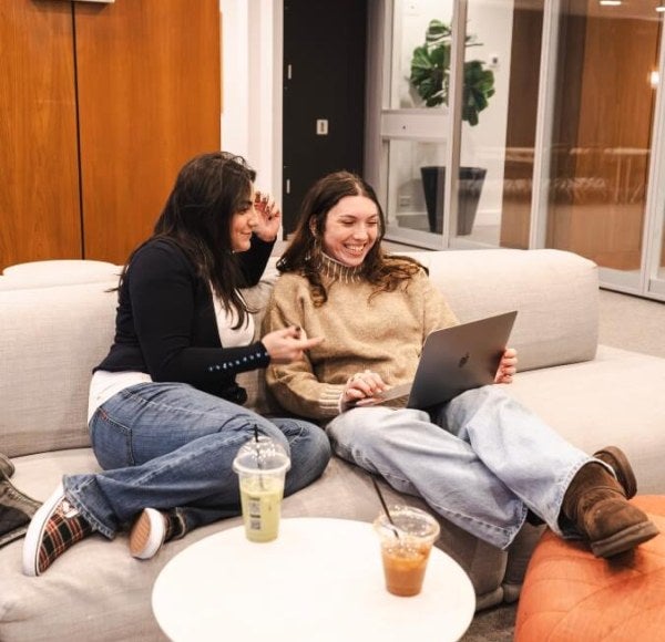Paige and Jenna sit on couch, looking at shared laptop in FOUND Study - Midtown East residence hall