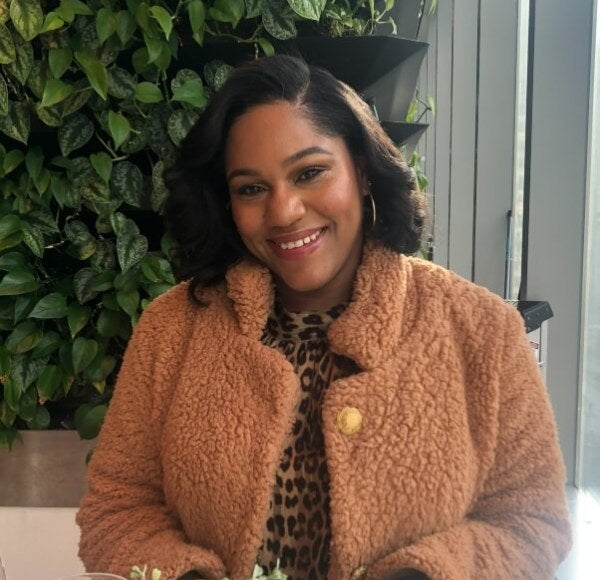 seated woman, shoulder-length dark hair, pink coat, foliage in background