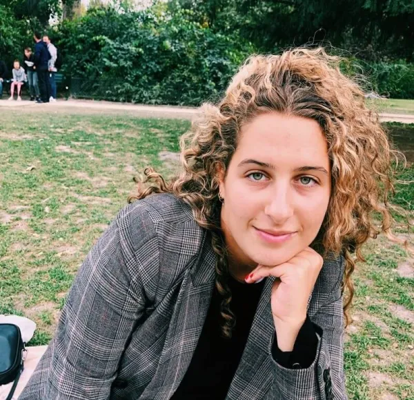 woman with blonde curly hair, gray blazer, sits in an outdoor park setting