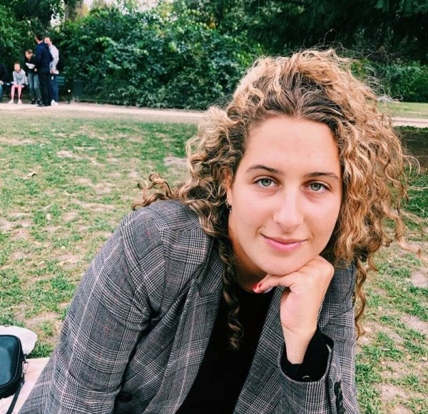 woman with blonde curly hair, gray blazer, sits in an outdoor park setting