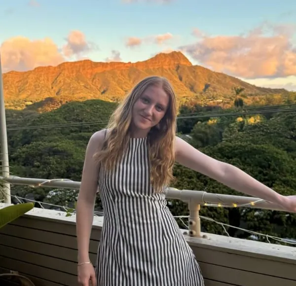 young woman, long red hair, outdoor balcony, mountains in background, vertical-striped dress