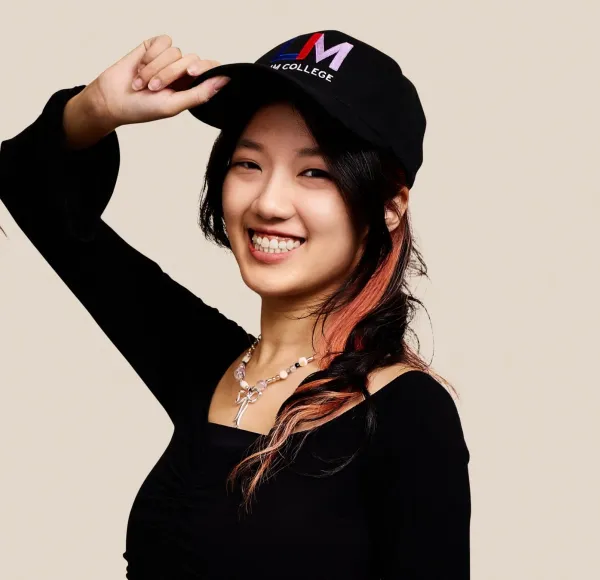 young woman, black long-sleeved shirt, LIM College hat, smiles at camera