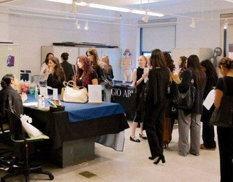 Full career fair room, professionally dressed students and young people, tables with employers and logo-bearing table cloths