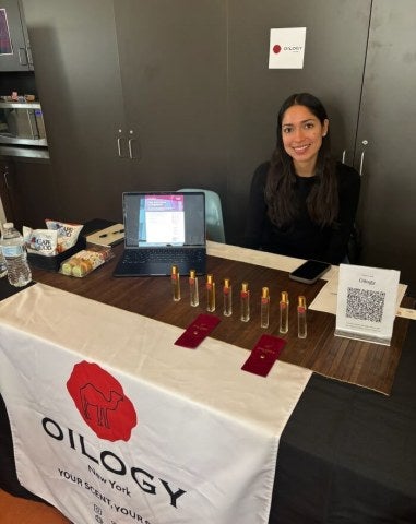 Oligy activation, career fair. Woman with long dark hair smiles at product giveaway table.
