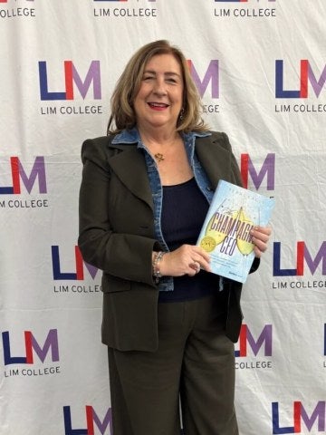 Terri Eagle holds book in front of LIM College step-and-repeat