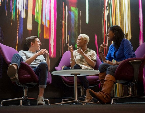 Three people talking in front of a brightly-colored wall.