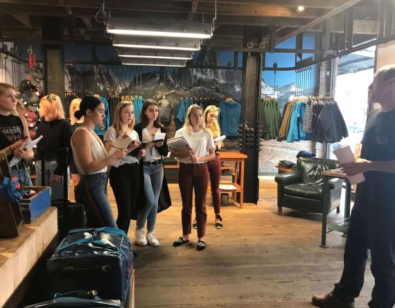 LIM students visit a Patagonia store. They take notes on notepads while a store employee gives a talk