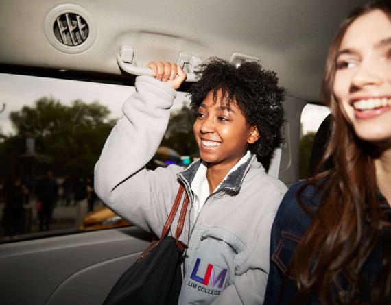 Two LIM students share a taxi in the busy streets of New York City. One student wears an LIM jacket