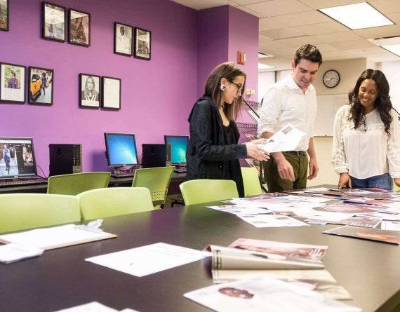 Three students look at magazine spreads on a table