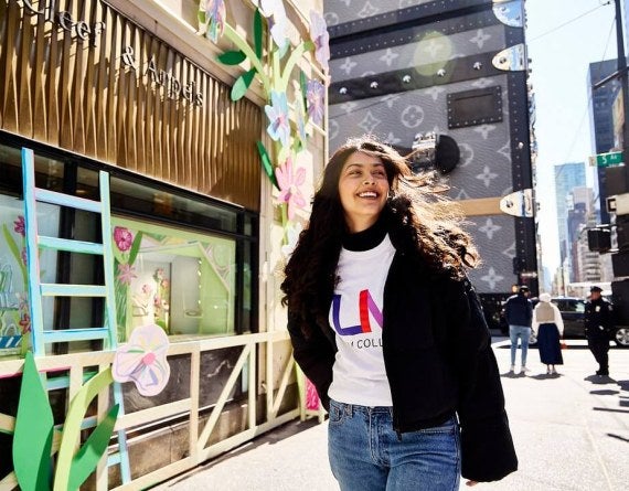 young woman, long dark hair, LIM shirt, walks near Fifth Avenue in NYC.