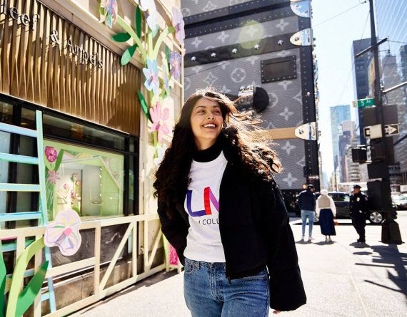 young woman, long dark hair, LIM shirt, walks near Fifth Avenue in NYC.