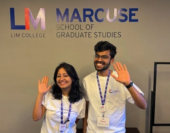 two students, one male one female, waving in the student lounge at LIM's Marcuse School of Graduate Studies.