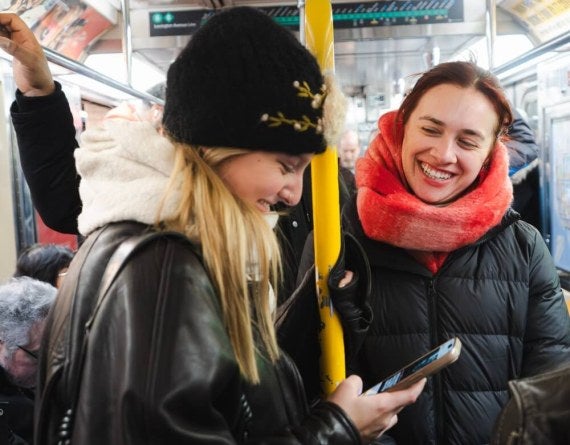 two young female students ride the New York City subway, smiling, winterwear
