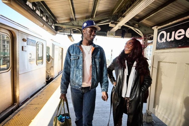 Two students, one in a denim jacket and one in a leather jacket, walk on the 7-train platform in Queens