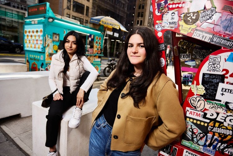 two students, one sitting and one leaning, are on the New York City sidewalk in Koreatown