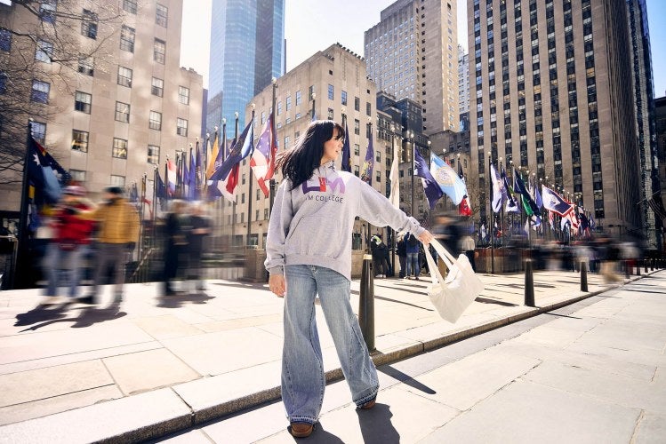 young woman, long dark hair, LIM sweatshirt, swinging bag, Rockefeller Center