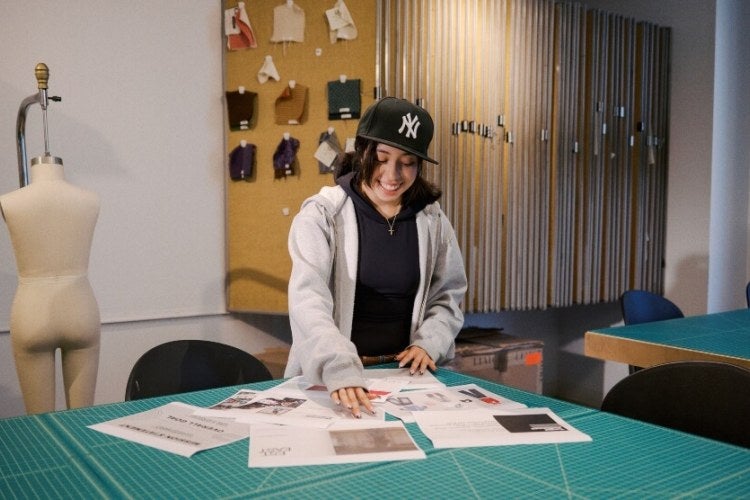 young woman, shoulder-length dark hair, Yankee ballcap, light-colored hoodie, fashion classroom