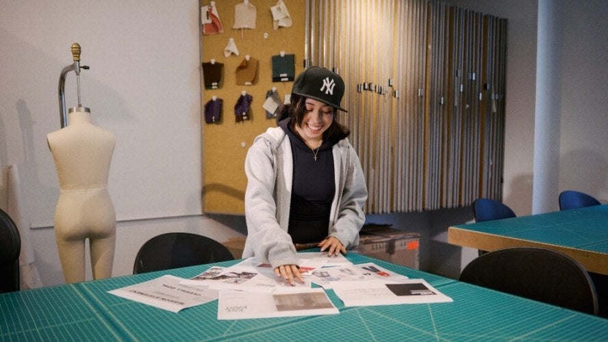 young woman, shoulder-length dark hair, Yankee ballcap, light-colored hoodie, fashion classroom