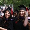 two graduating students smiling, side by side in outdoor College Commencement environment