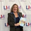 Terri Eagle holds book in front of LIM College step-and-repeat