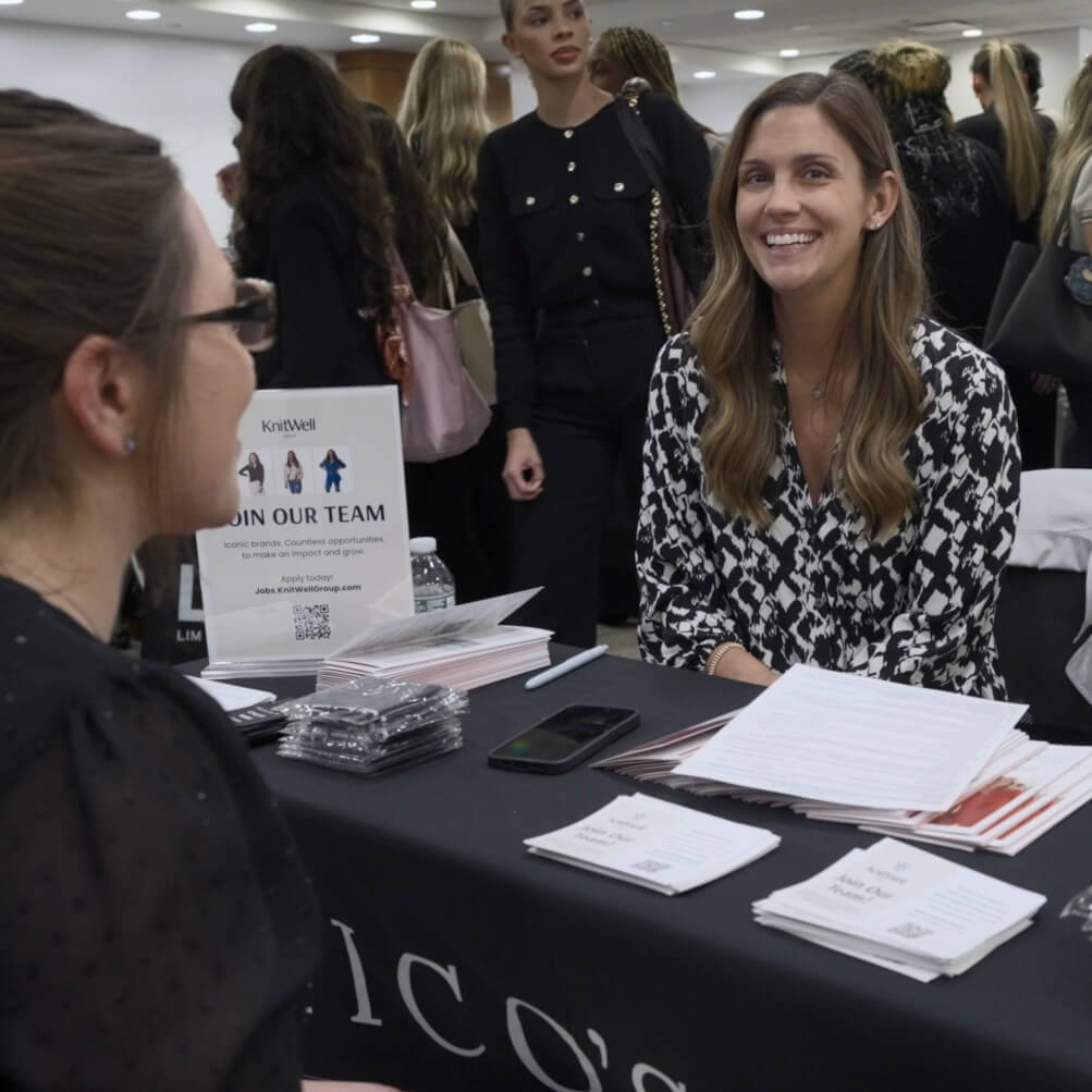 woman with long brown hair, black and white blouse, at a career fair table