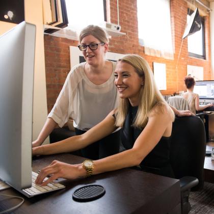 two women working on a computer together in an opened office