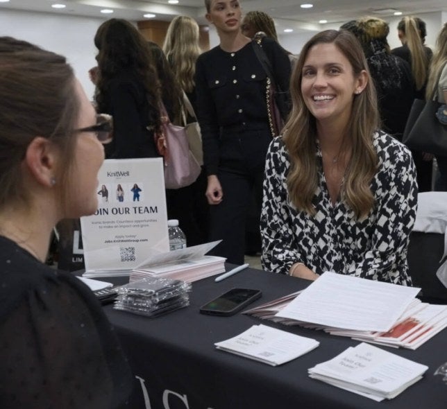 woman with long brown hair, black and white blouse, at a career fair table