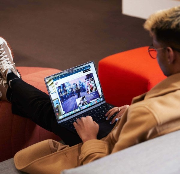 An LIM student sits on a lounge while on his laptop, which is open to the LIM website