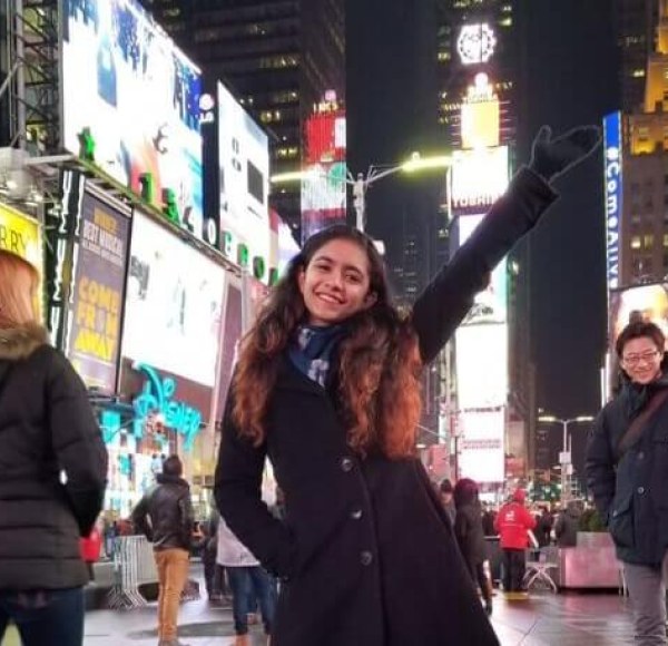 A female student raises her hand in the air while posing at Times Square in New York City